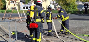 Feuerwehr  Hier sehen Sie vier Feuerwehrleute in Uniform und Ausrüstung beim verbinden zweier Löschschläuche.