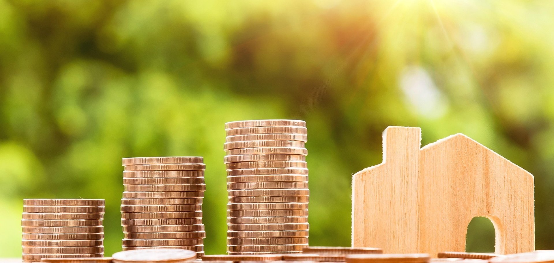 Hier sehen Sie Stapel aus Münzen neben einer Hausminiatur.