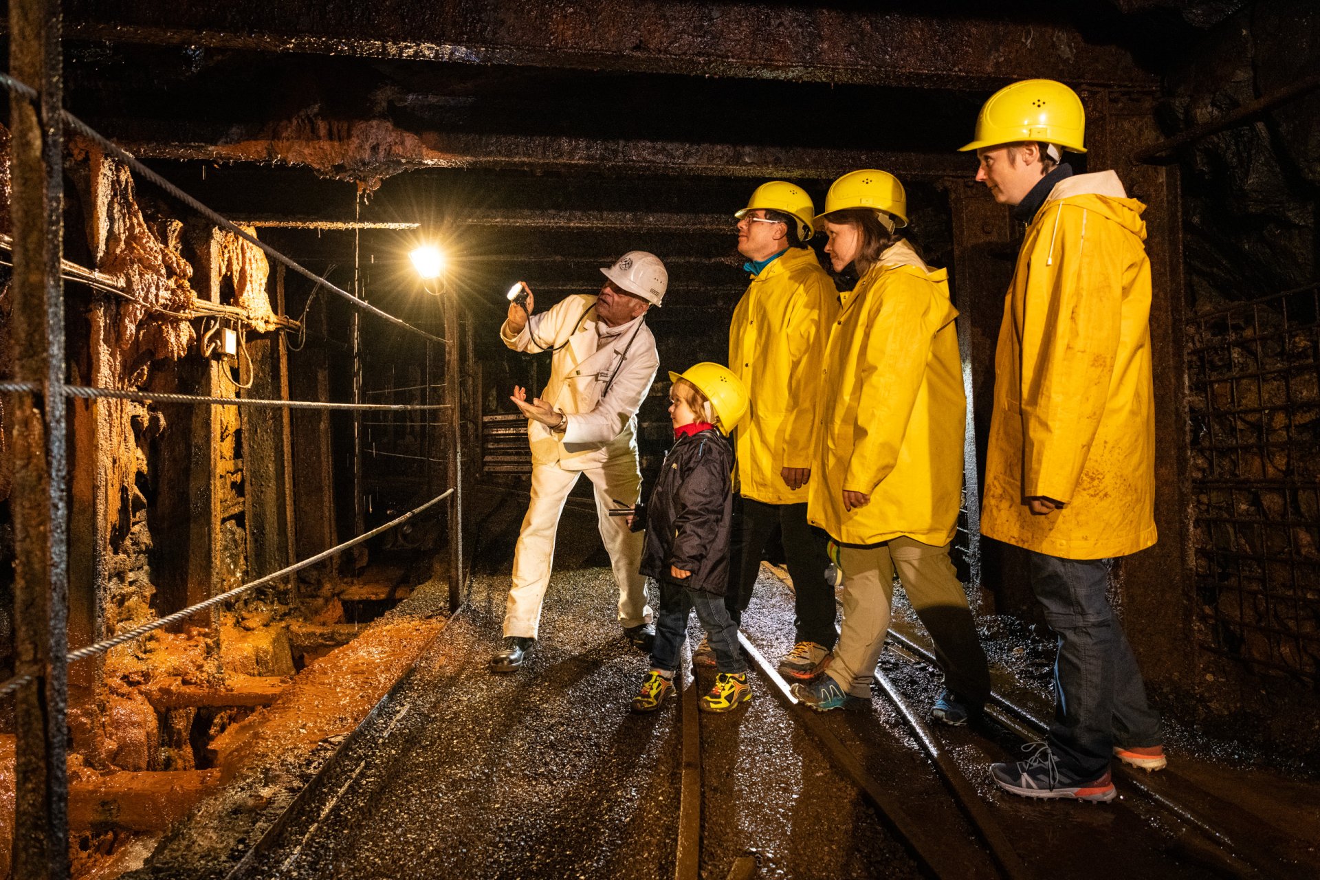 Besuchergruppe in der Grube Bindweide mit Taschenlampen, Schutzhelm und gelben Regenjacken im Stollen.
