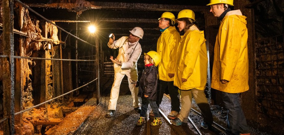 Besuchergruppe in der Grube Bindweide mit Taschenlampen, Schutzhelm und gelben Regenjacken im Stollen.