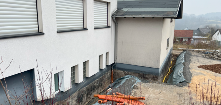 Hier sehen Sie die sanierungsbedürftige Stelle am Sockel des Bauhofgebäudes in Weitefeld vom oberen Parkplatz aus.