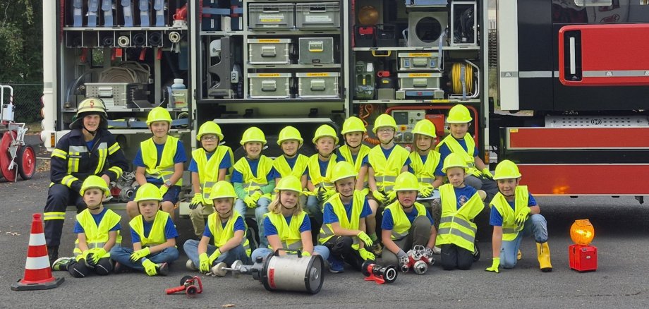 Hier sehen Sie eine Gruppe von Kindern in Feuerwehruniformen vor einem Feuerwehrauto.