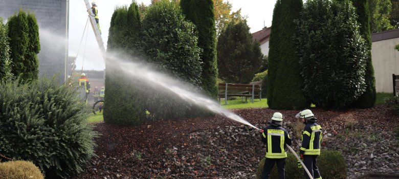 Hier sehen Sie zwei Feuerwehrleute die einen Schlauch halten aus dem Wasser spritzt.