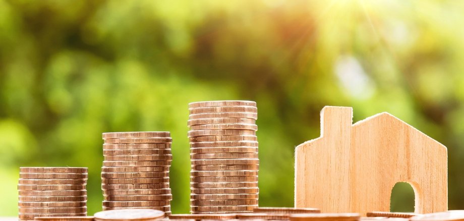 Hier sehen Sie Stapel aus Münzen neben einer Hausminiatur.