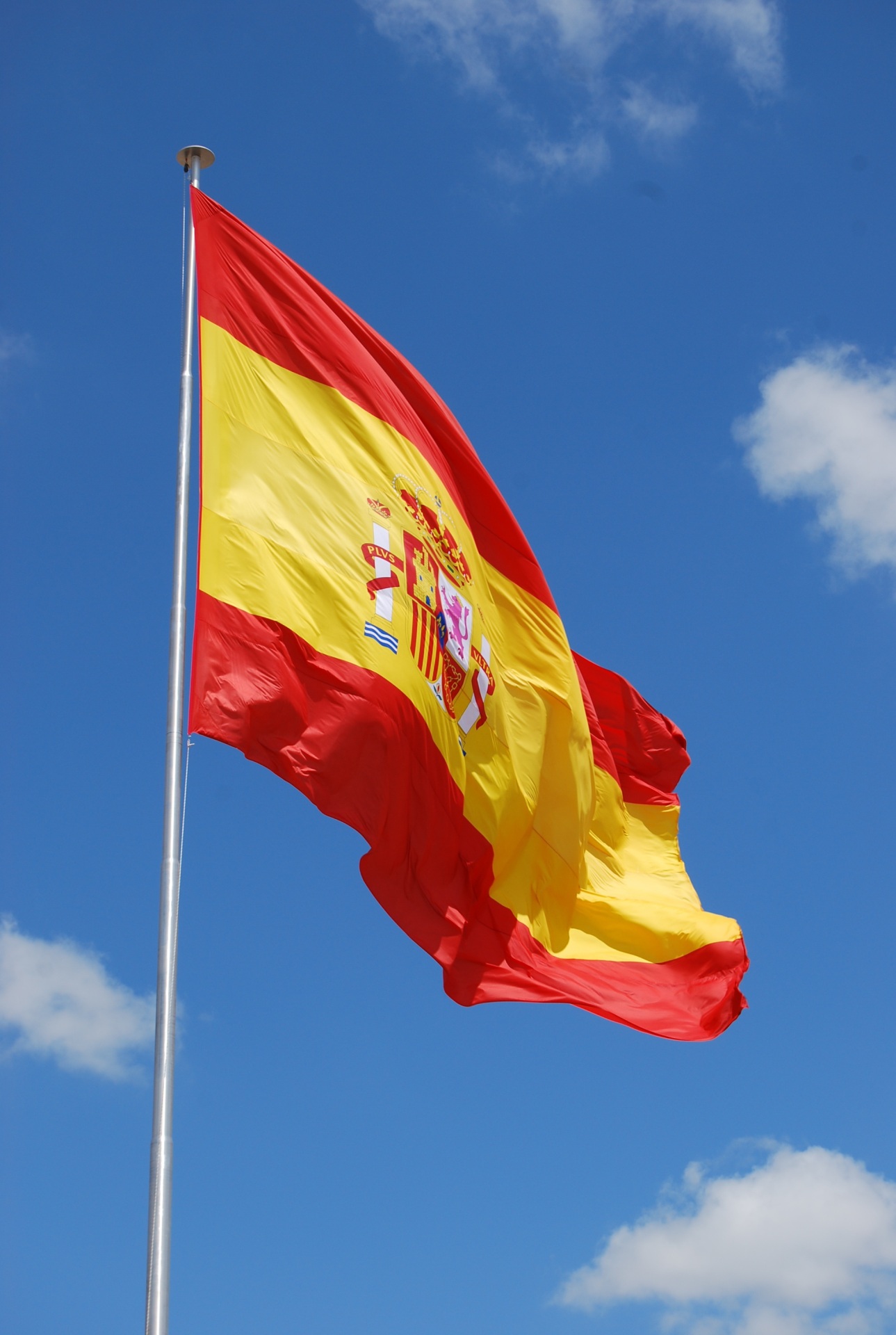 Hier sehen Sie die Flagge von Spanien vor blauem Himmel.