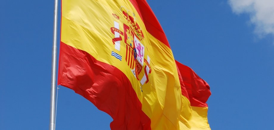 Hier sehen Sie die Flagge von Spanien vor blauem Himmel.
