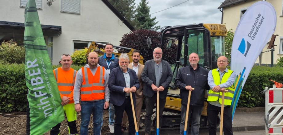 Hier sehen Sie Alessandar Chergovski (Bauleiter MIH), Nermin Kurahovic (Projektleiter MIH), Dustin Kocaa (Panda Promotion), Helmut Stühn (Bürgermeister), Sezer Carikci (Projektmanager FttH Vertrieb), Walter Strunk (Stadtbürgermeister Daaden), Dirk Peschel (Senior Manager kommunale Kooperationen), Eungseok Lee (Projektmanager Bau) beim Spatenstich zum Glaserfaserausbau in der Stadt Daaden durch die Deutsche Glasfaser.