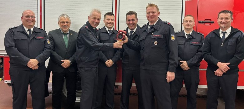  Symbolische Weitergabe eines Strahlrohrs: Matthias Theis (Wehrleiter), Helmut Stühn (VG-Bürgermeister), Jörg Hölzemann, Robin Pankow, Kay Strunk, Florian Knautz, Heiko Lichtenthäler (stv. Wehrleiter), Volker Hain (Vorsitzender KFV) vor einem Feuerwehrauto bei der Feuerwehr Weitefeld.