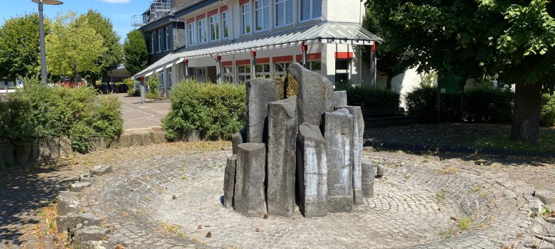 Hier sehen Sie den Dorfbrunnen von Weitefeld und im Hintergrund die Grundschule