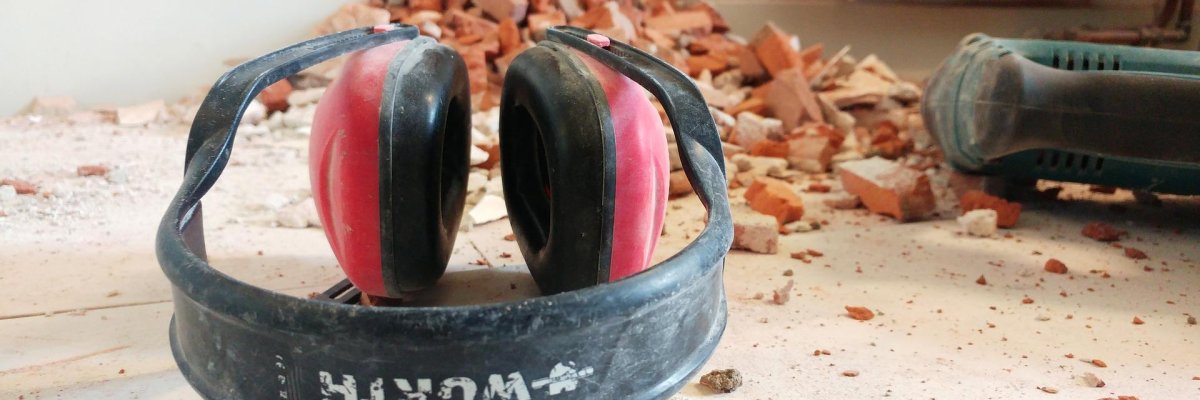 Bauen Hier sehen Sie einen Ohrschützer und einen Vorschlaghammer auf einer Baustelle liegen.