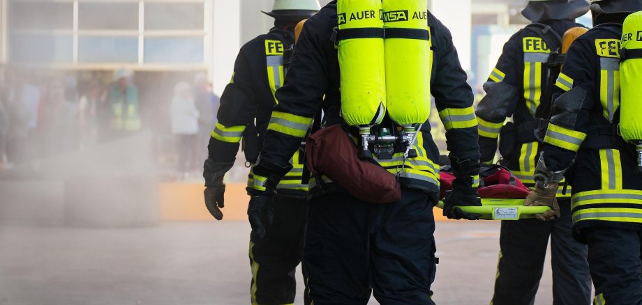 Hier sehen Sie vier Feuerwehrleute die eine Krankentrage tragen