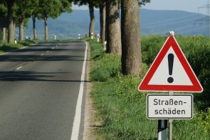 Straßenschäden Hier sehen Sie das Verkehrsschild "Allgemeine Gefahrenstelle" mit dem Hinweis "Straßenschäden" und im Hintergrund eine Landstraße.