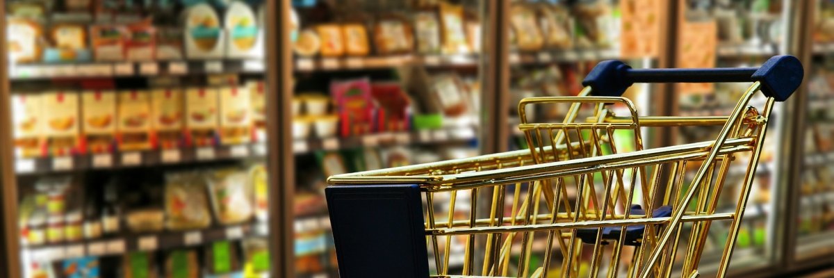 Hier sehen Sie einen leeren Einkaufswagen vor einem Supermarktregal.